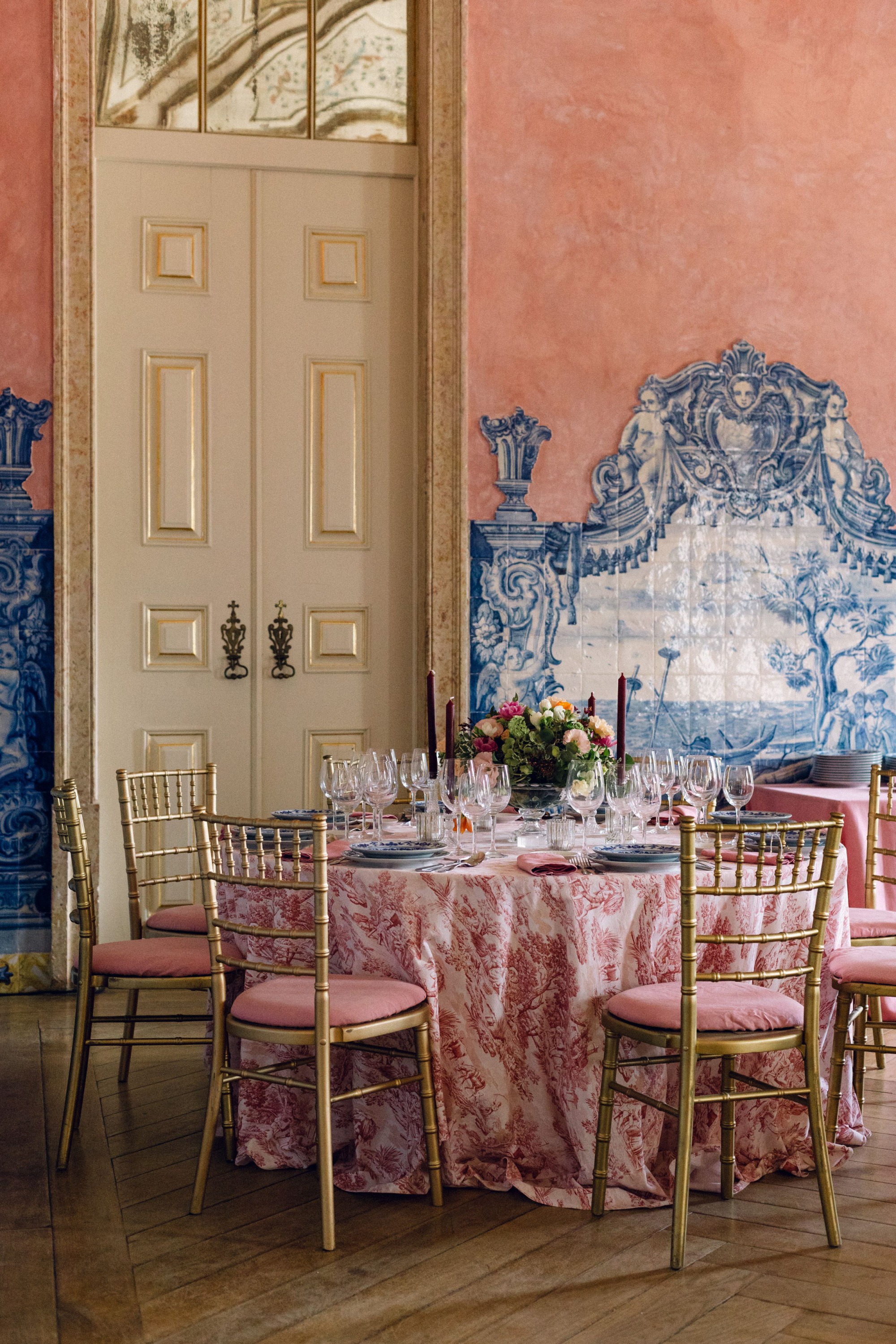 Elegant dining room with blue tile walls and pink tablecloths set for a formal event.